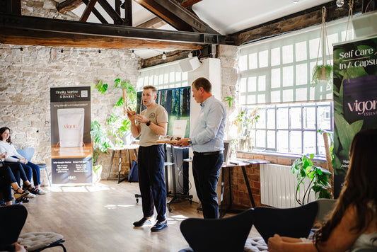 Two men in a modern office setting with plants and promotional banners. 28