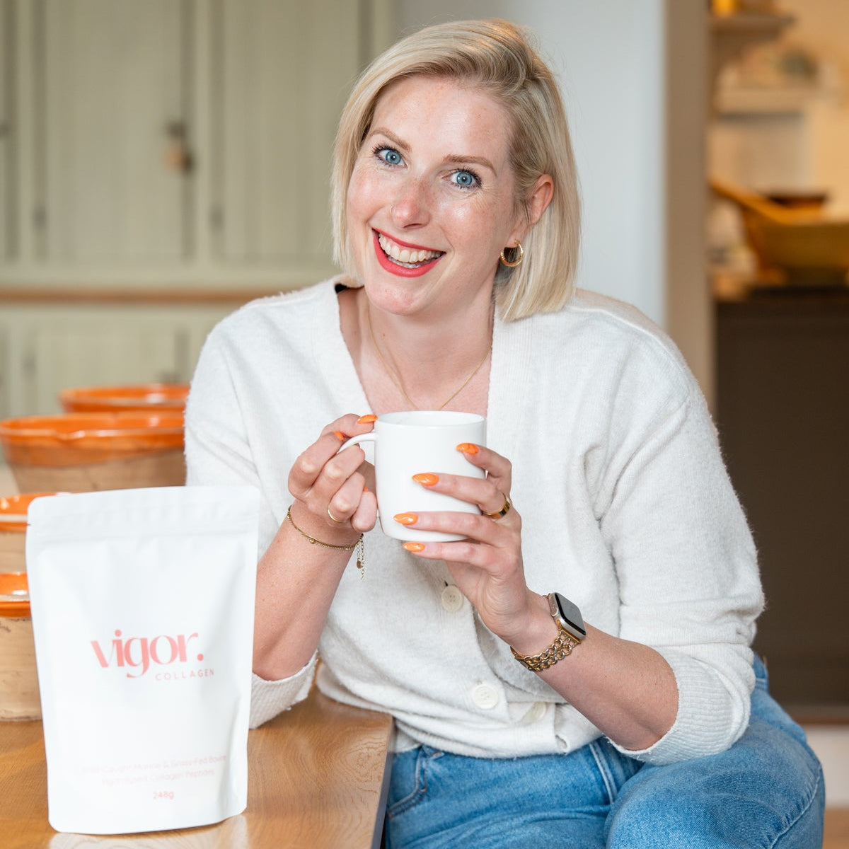 Woman holding a white mug with 'VIJOG' branding in a kitchen setting.