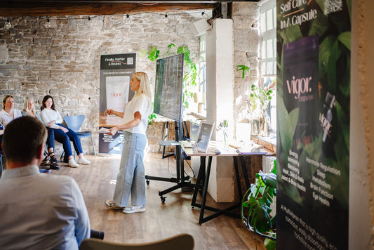 Rachel Woolford giving a presentation in a casual office setting with 'Vigor' branding. 23