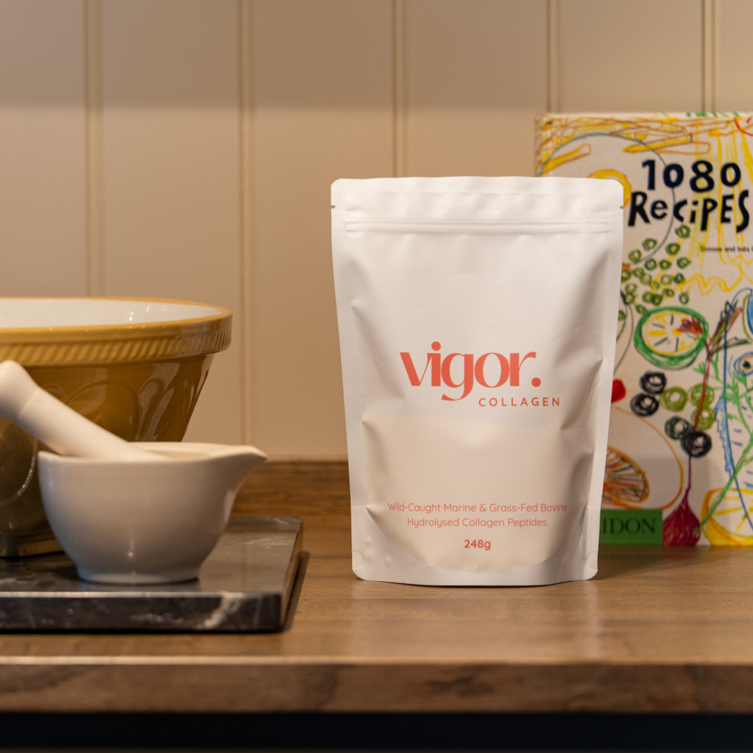 Vigor collagen package on a wooden surface with kitchen items and a cookbook in the background.